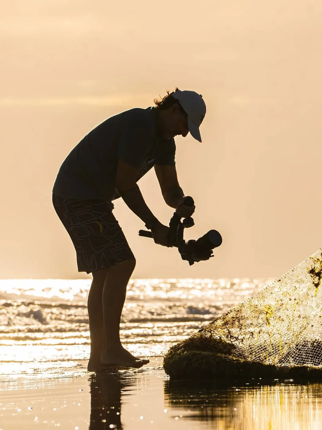 Fotógrafo em contraluz trabalhando na beira da praia, no fim de tarde